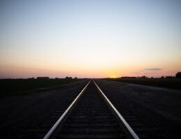 Gerade Bahnstrecke führt bei Sonnenuntergang durch ländliche Felder
