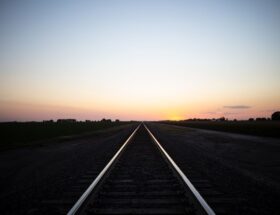 Gerade Bahnstrecke führt bei Sonnenuntergang durch ländliche Felder