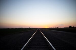 Gerade Bahnstrecke führt bei Sonnenuntergang durch ländliche Felder