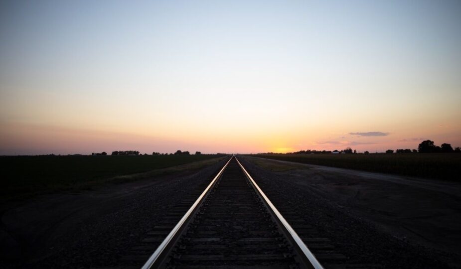 Gerade Bahnstrecke führt bei Sonnenuntergang durch ländliche Felder